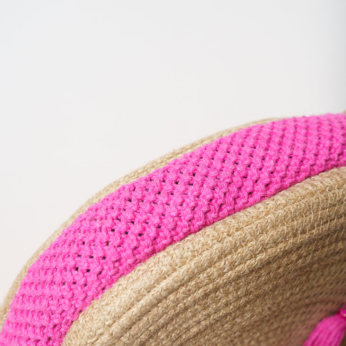 Close-up detail of a woven straw hat with a bright pink crocheted band, showing the texture of both materials against a light gray background.